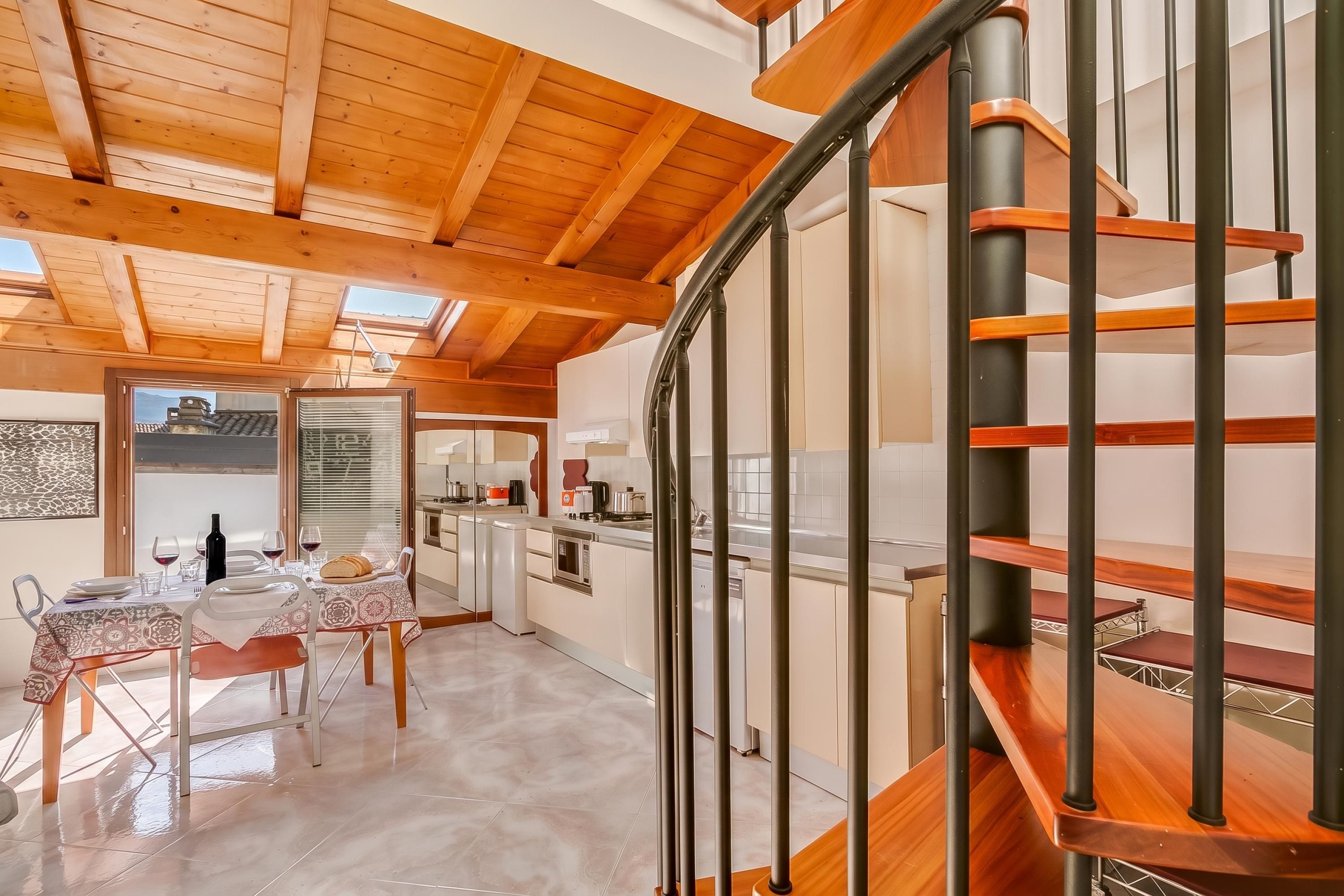 Une cuisine moderne avec des meubles blancs, un escalier en bois et un coin repas avec une table mise pour deux personnes.