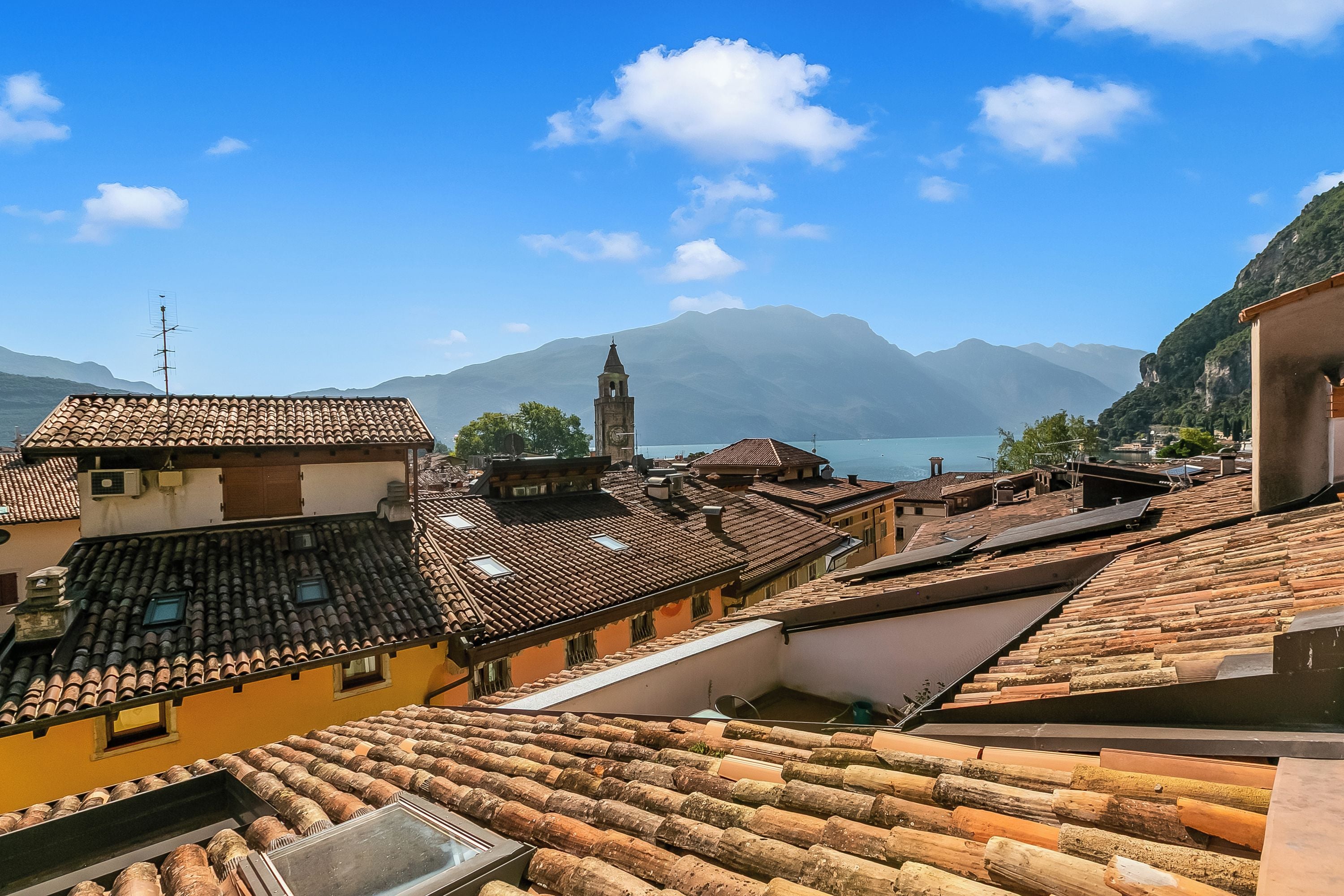 A view of terracotta-tiled rooftops, a prominent clock tower, and a mountain range in the background.