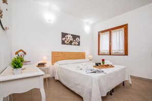 A hotel room with a bed, bedside table, lamp, potted plant, and a window with curtains. - Casa Angela With Pool (Olbia)