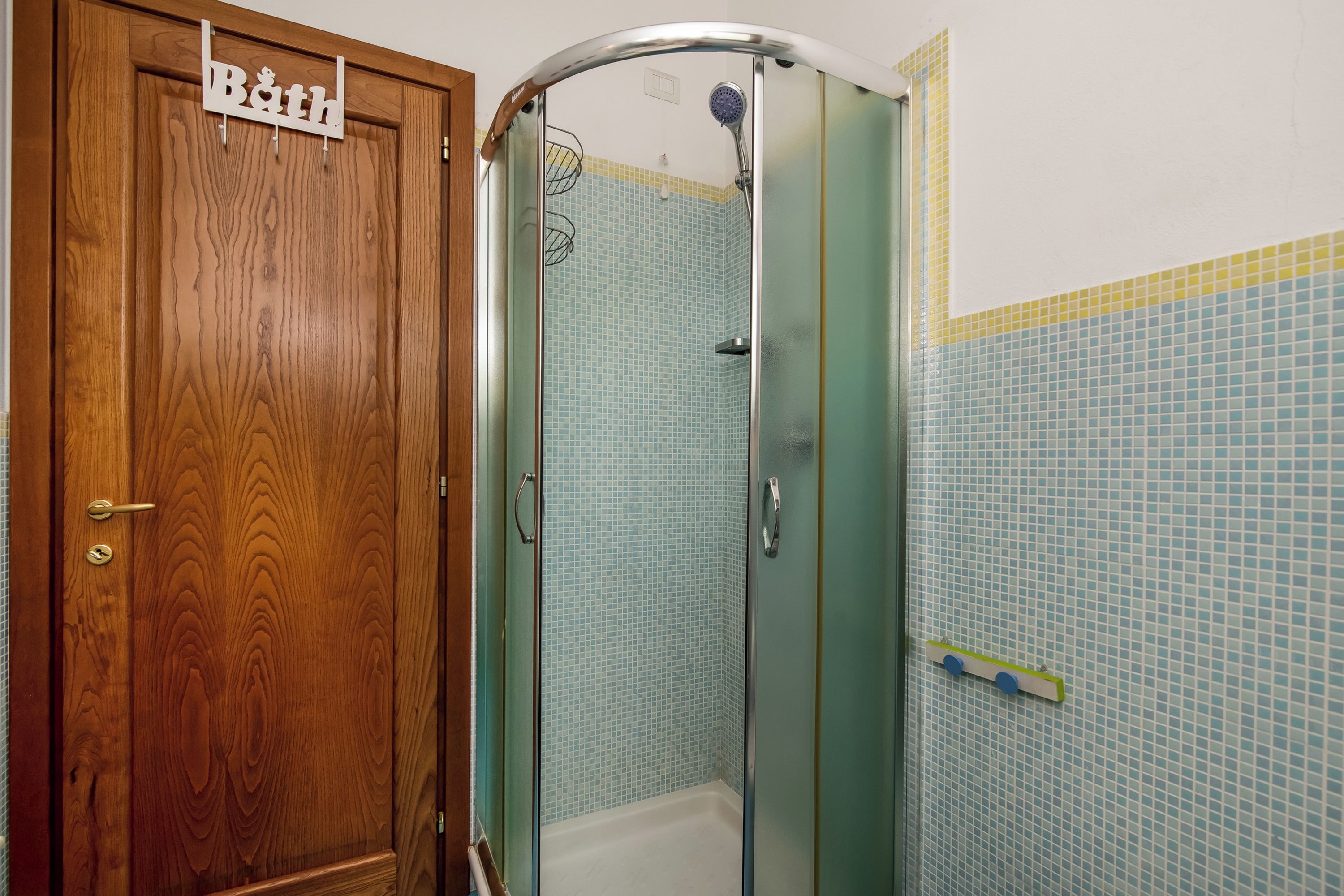 Een badkamer met een houten deur, een douchecabine en betegelde wanden.