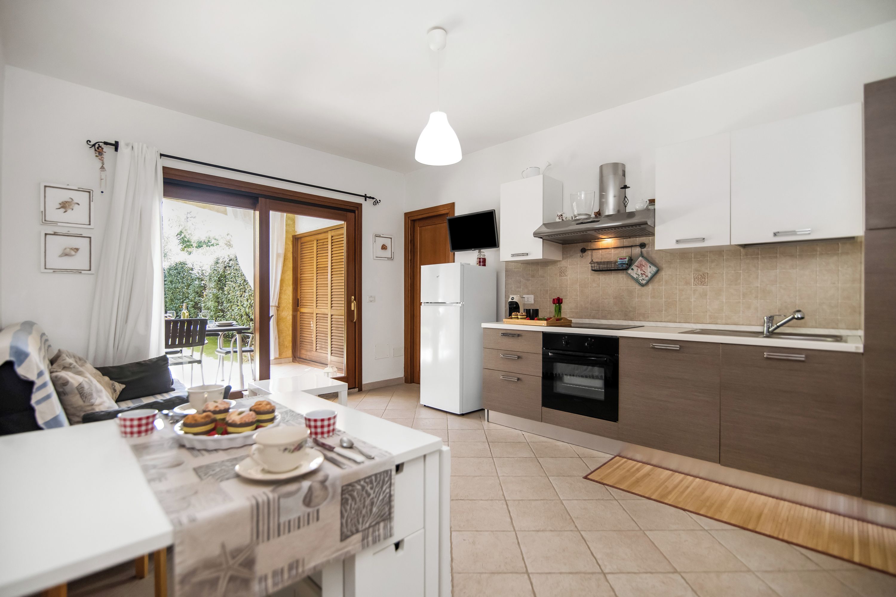A modern kitchen with white cabinets, a built-in oven, and a dining area with a table set for a meal.