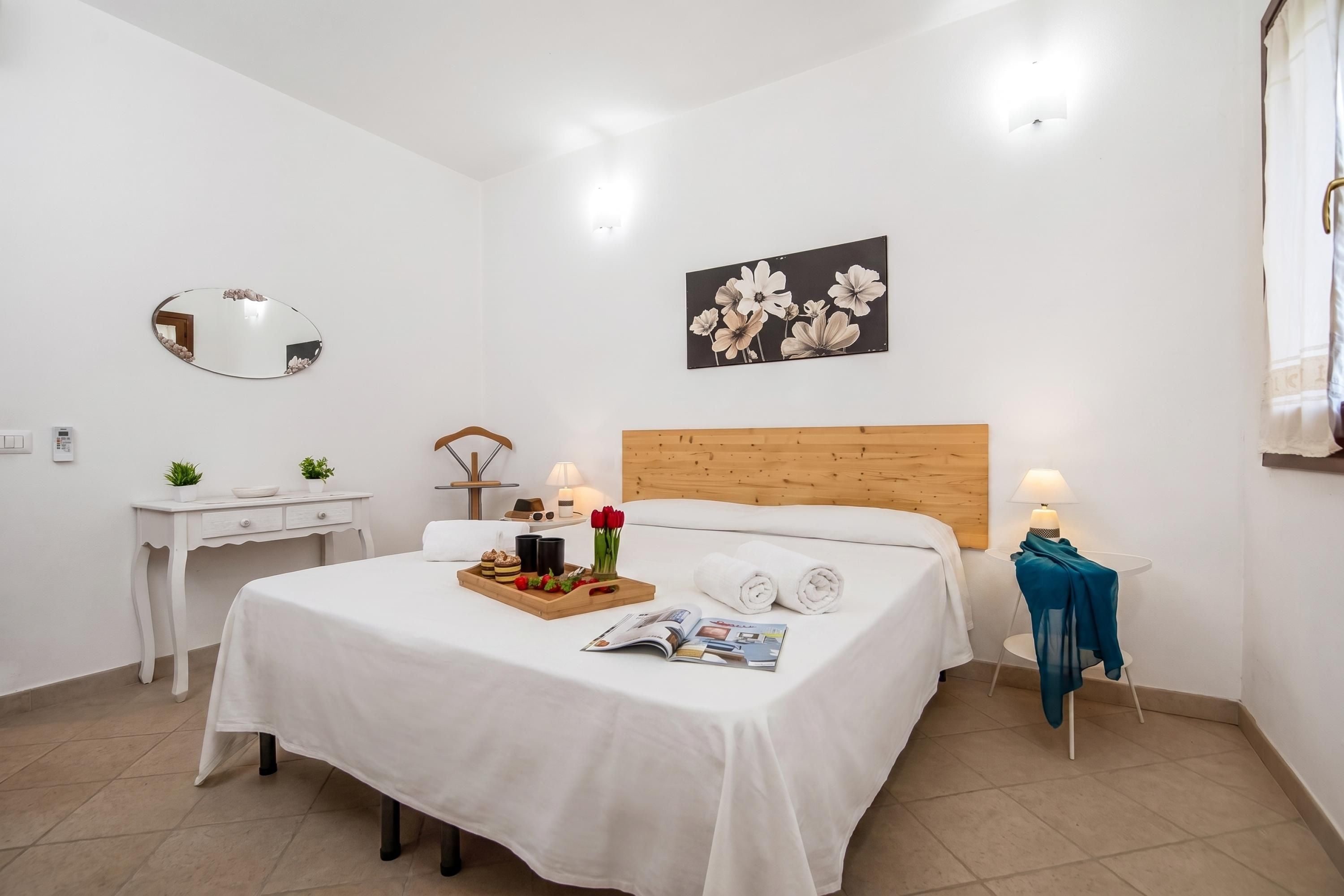 A hotel room with a bed, bedside table, lamp, and a painting on the wall.
