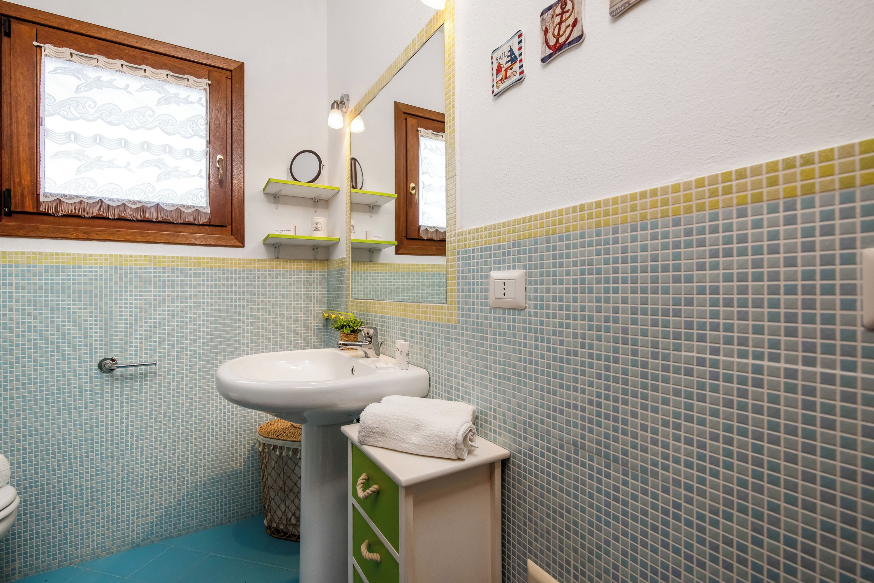 A bathroom with a white sink, a mirror, a towel, and a window with a lace curtain.