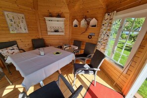 L’intérieur d’un chalet en bois comprend une table à manger, des chaises, un petit coin cuisine et une fenêtre donnant sur un paysage verdoyant.