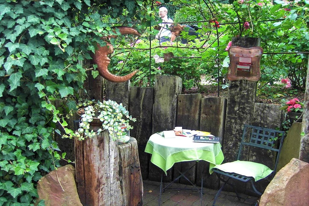 A garden with a table and chairs, surrounded by greenery and a wooden fence.