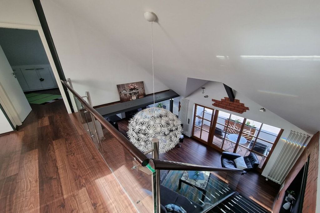 Un'ampia zona giorno con soffitto alto, un grande lampadario decorativo e vista sull'esterno attraverso ampie finestre.