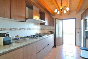 A kitchen with wooden cabinets, a gas stove, and a window leading to a bright outdoor area. - Finca in Muro with swimming pool (Muro)