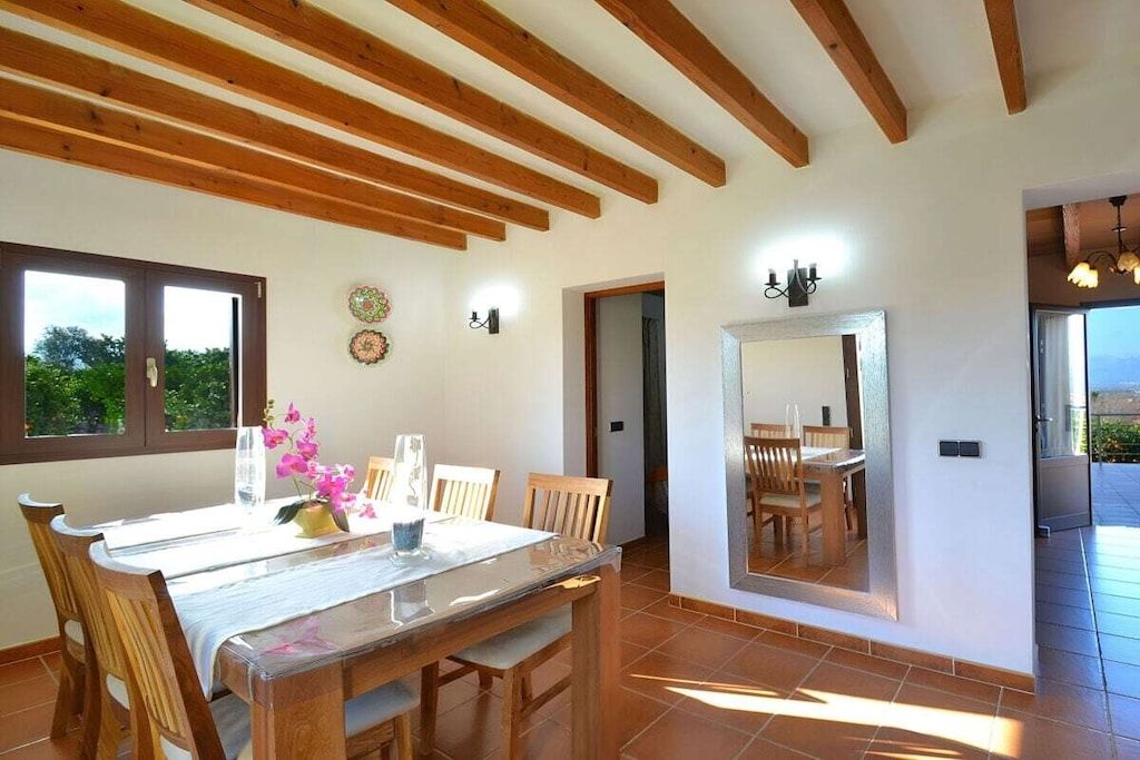 Un comedor con vigas de madera, una mesa con sillas, un espejo y vistas por una ventana.