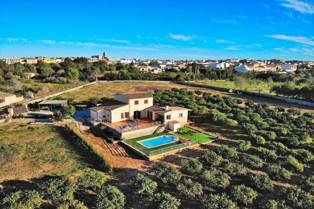 Une maison à deux étages avec une piscine, entourée d’oliviers et sous un ciel dégagé.