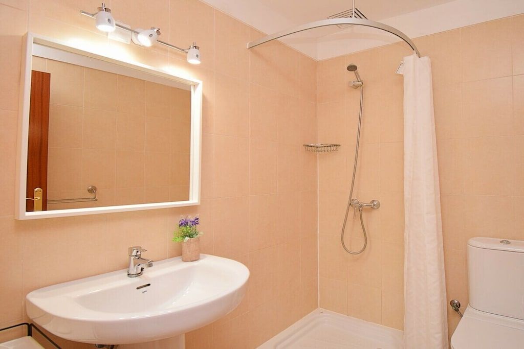 A bathroom with a white sink, a mirror, a shower with a curtain, and a toilet.