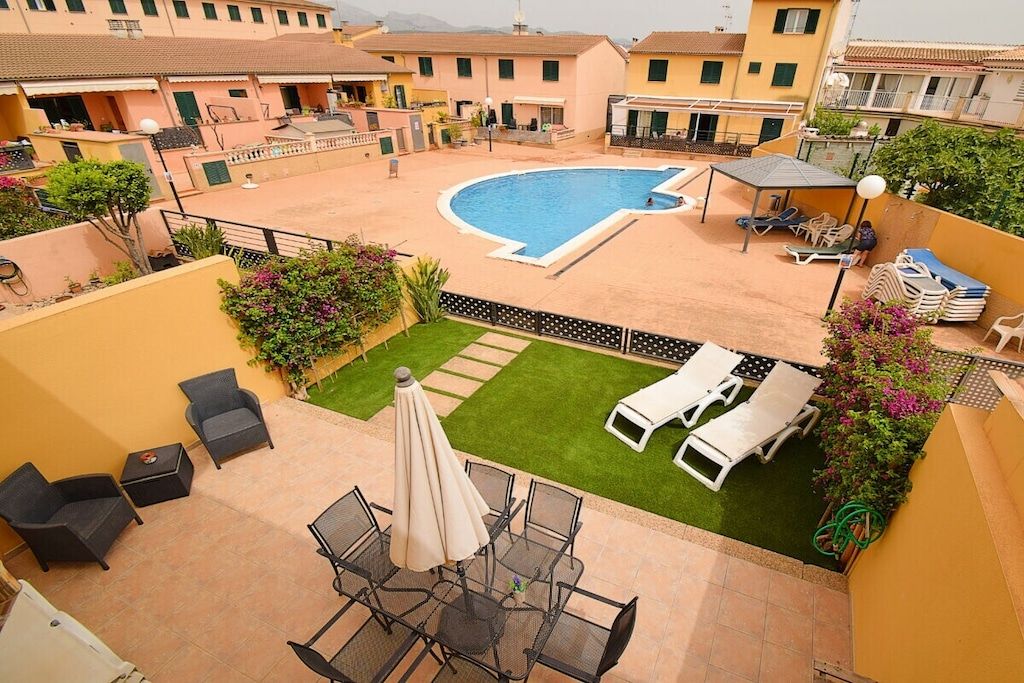 A rooftop pool area with lounge chairs, a table, and a small garden.