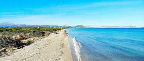 A beach with a clear sky, calm sea, and distant mountains.