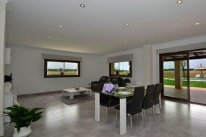 A modern living room with a dining area, large windows, and a view of the outdoors.