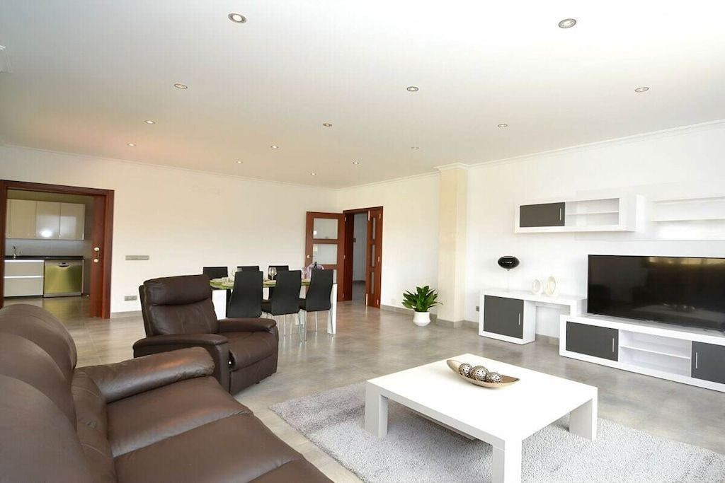 A modern living room with a sofa, a coffee table, a TV, and a dining area with chairs and a table.