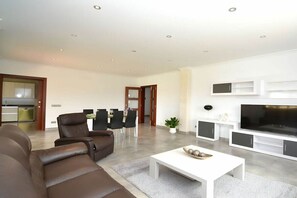 A modern living room with a sofa, a coffee table, a TV, and a dining area with chairs and a table.