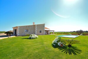 A stone house with a swimming pool, surrounded by a well-maintained lawn and flowering plants.