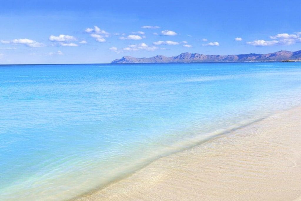 A beach with clear blue water and a distant mountain range.