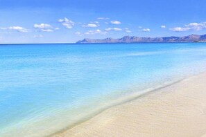 A beach with clear blue water and a distant mountain range.
