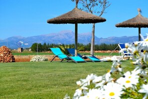 A grassy area with two thatched umbrellas, a windmill, and a mountain backdrop.