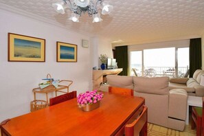 A room with a wooden dining table, a beige sofa, and a view of the sea through large windows. - Apartment in Alcudia with terrace (Alcudia)