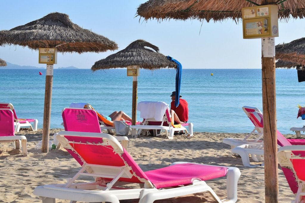 Una playa con sombrillas de paja, sillas de descanso y una vista despejada del mar.