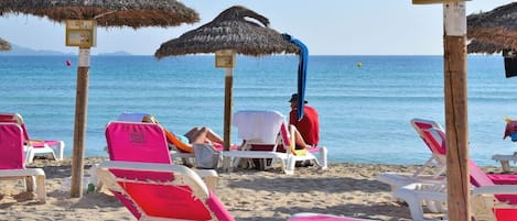 Una playa con sombrillas de paja, sillas de descanso y una vista despejada del mar.