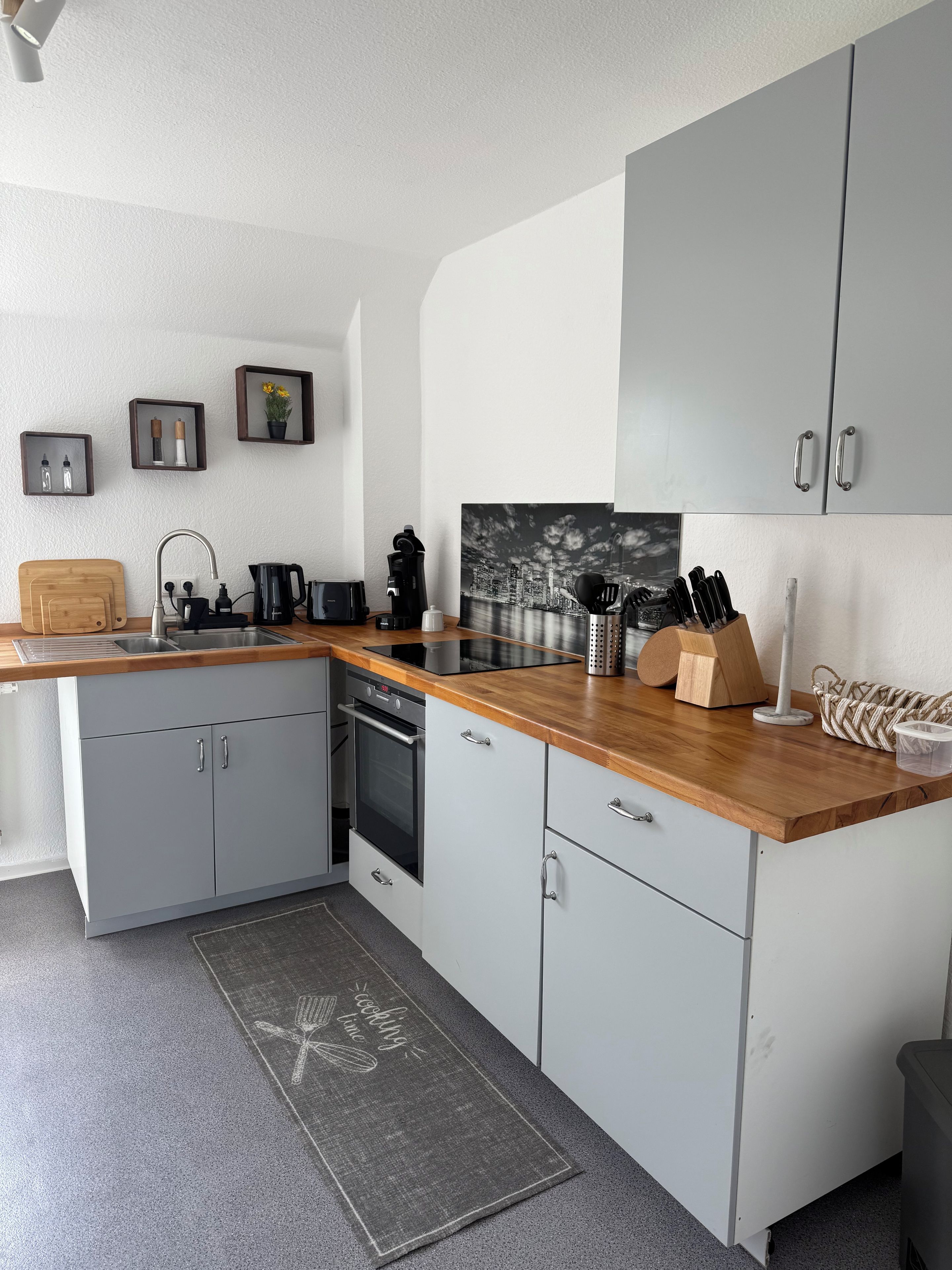 A modern kitchen with grey cabinetry, a wooden countertop, and various kitchen appliances.