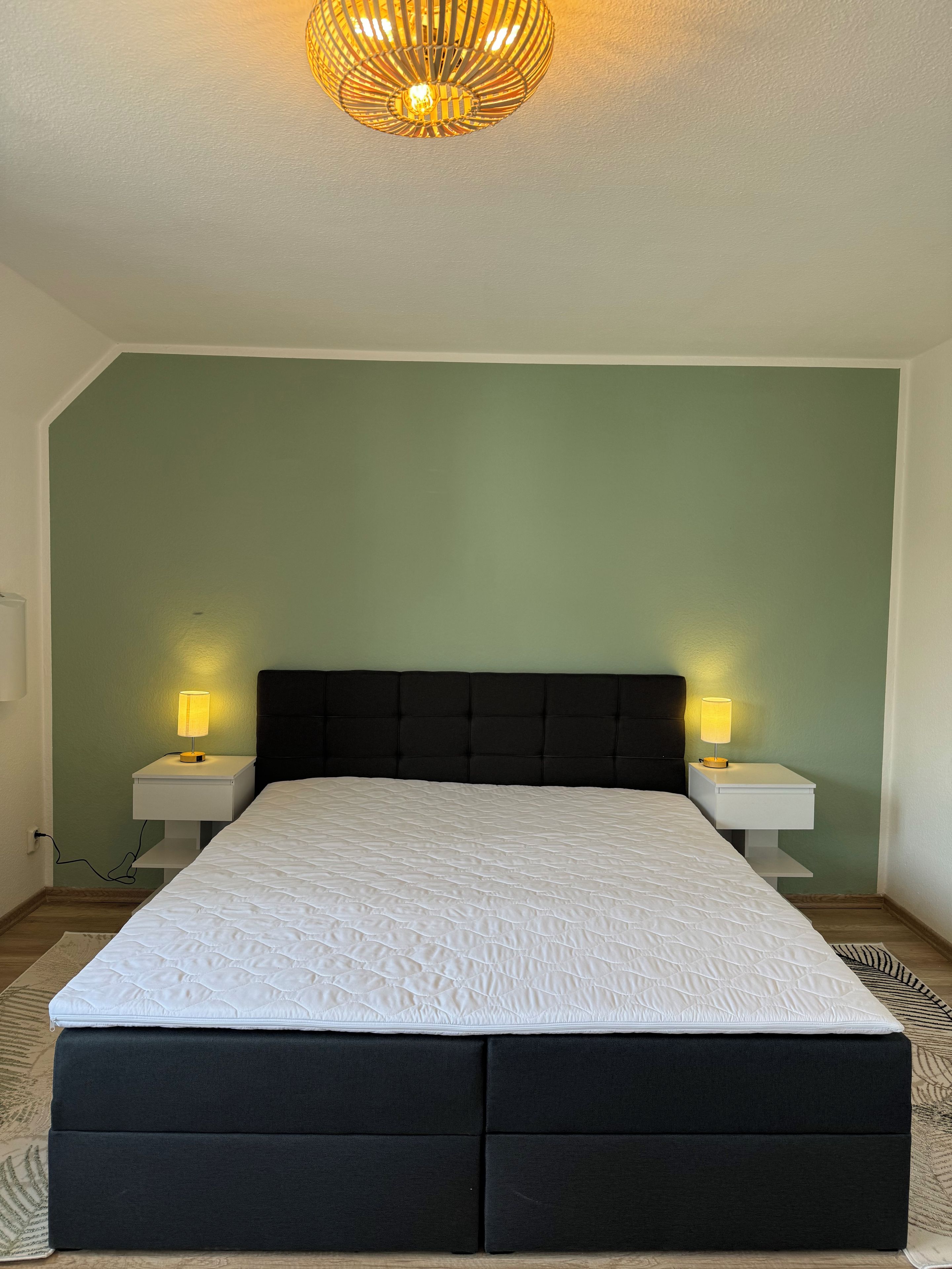Un dormitorio con cama, dos mesitas de noche con lámparas y un candelabro en el techo.