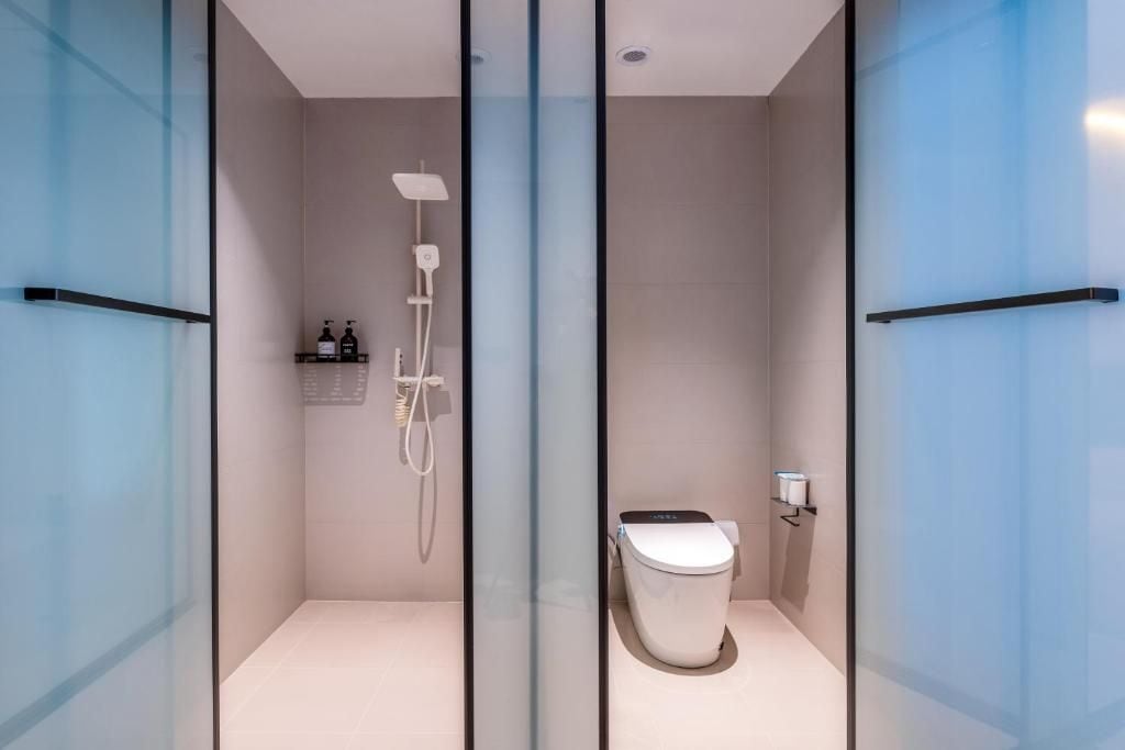 Un baño moderno con ducha envuelta en vidrio, un inodoro y un estante con artículos de aseo.