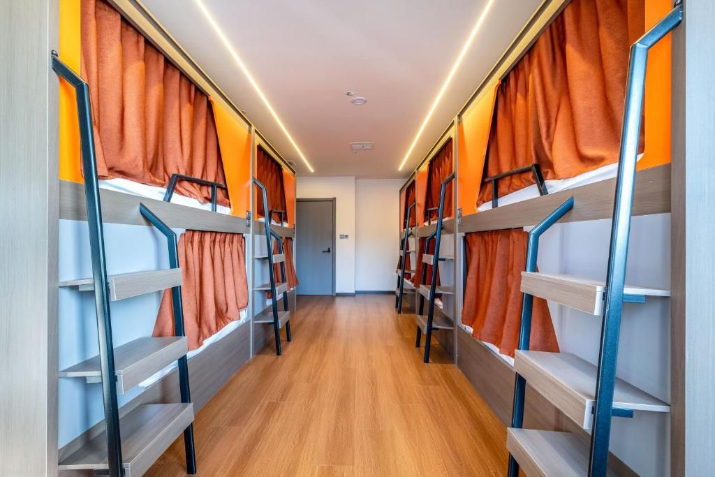 Um corredor com beliches em ambos os lados, piso de madeira e cortinas laranja.
