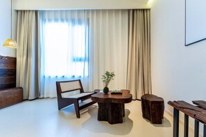 A room with a wooden bench, a round table with a plant, and a large window with curtains.