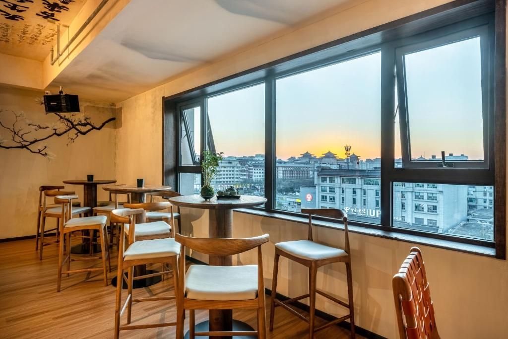 A room with a view of a cityscape through large windows, wooden chairs, and a small table with a plant.