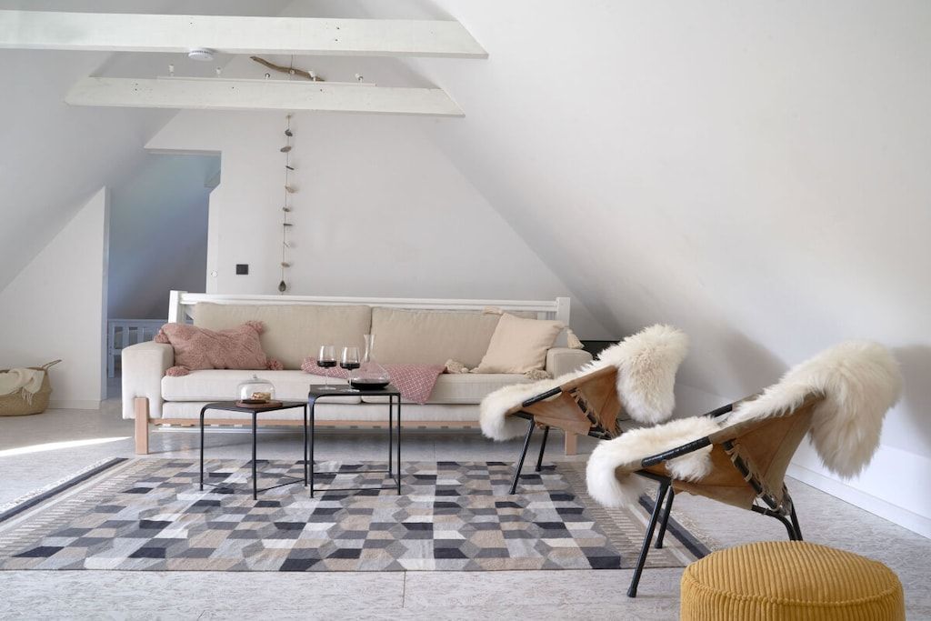 Ein modernes Schlafzimmer im Loft-Stil mit schrägem Dach, einem großen Fenster, einer Couch, einem Couchtisch und einem Sessel mit Fellbesatz.