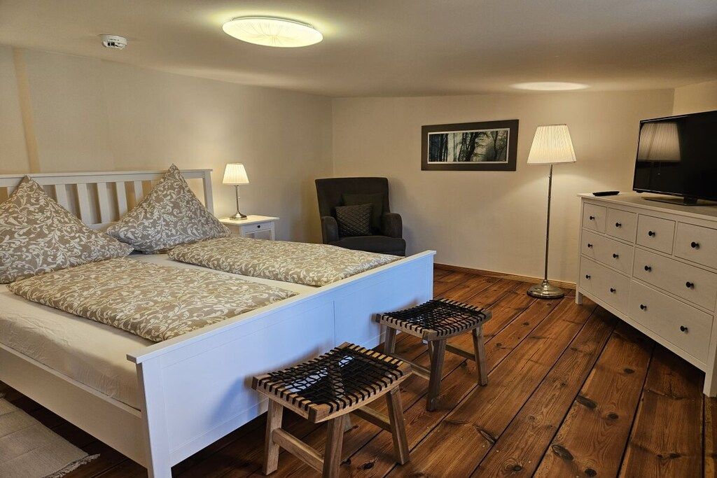 Une chambre à coucher comprenant un lit, des tables de chevet, une chaise, un téléviseur et une commode.