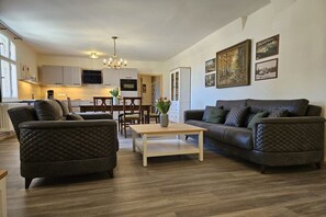 A modern living room with a dark leather sofa, a wooden coffee table, and a dining area with a chandelier. - "To the Harbor Master No. 1" (Lübbenau\/Spreewald)
