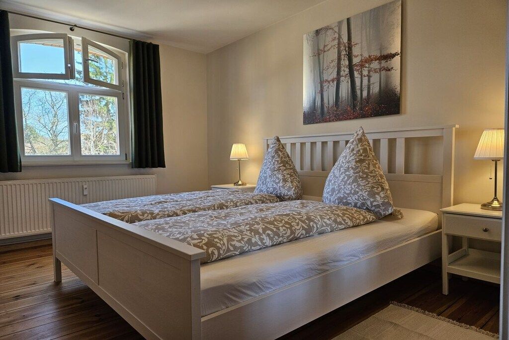 Un dormitorio con una cama doble, dos mesitas de noche, una ventana con cortinas y un cuadro en la pared.
