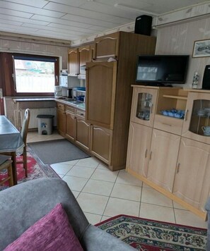 A compact kitchen with wooden cabinets, a dining table, and a television. - Holiday apartment with 2 bedrooms (Dornumersiel)