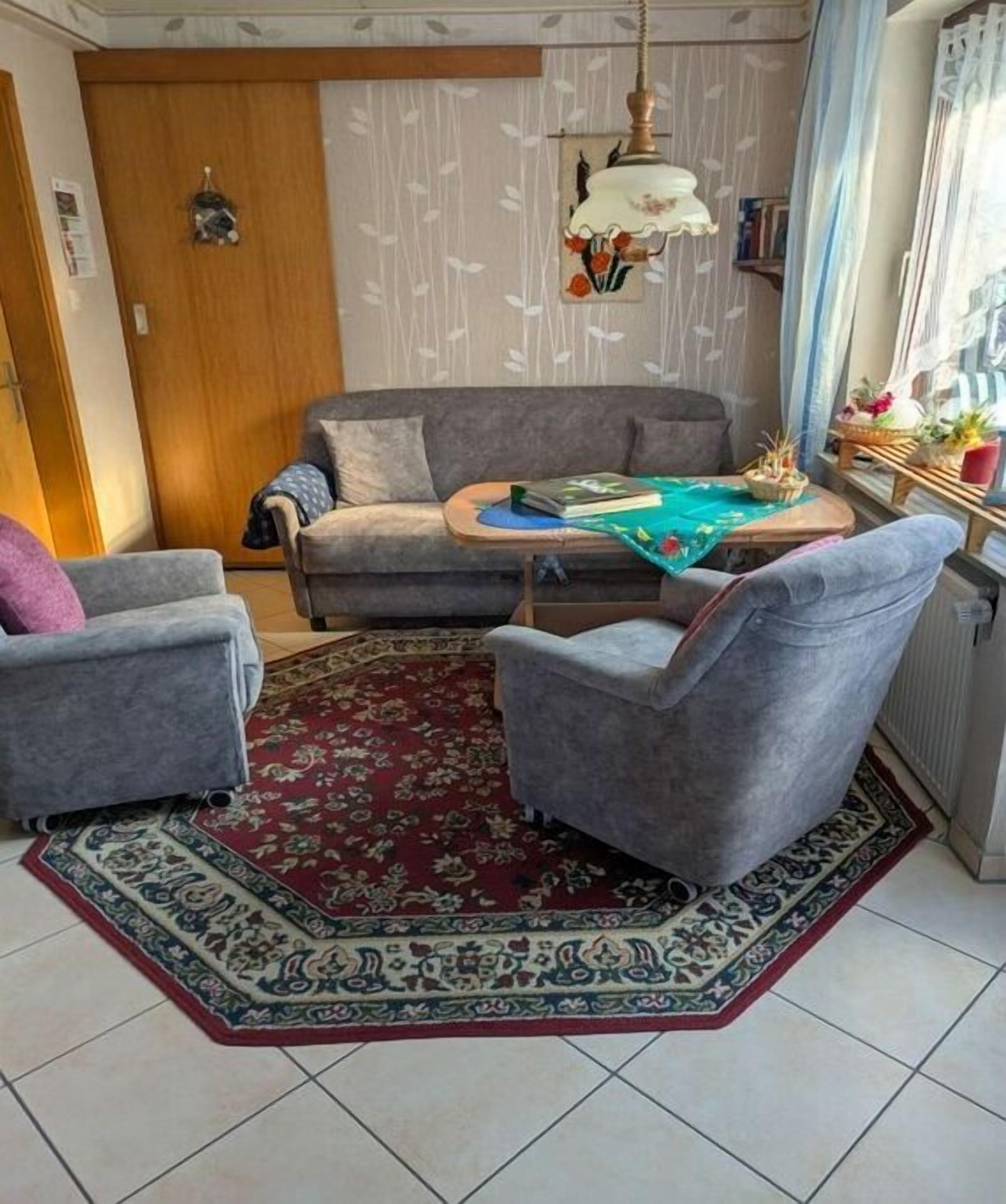 Ein Wohnzimmer mit einem grauen Sofa, zwei Sesseln, einem Couchtisch und einem gemusterten Teppich.