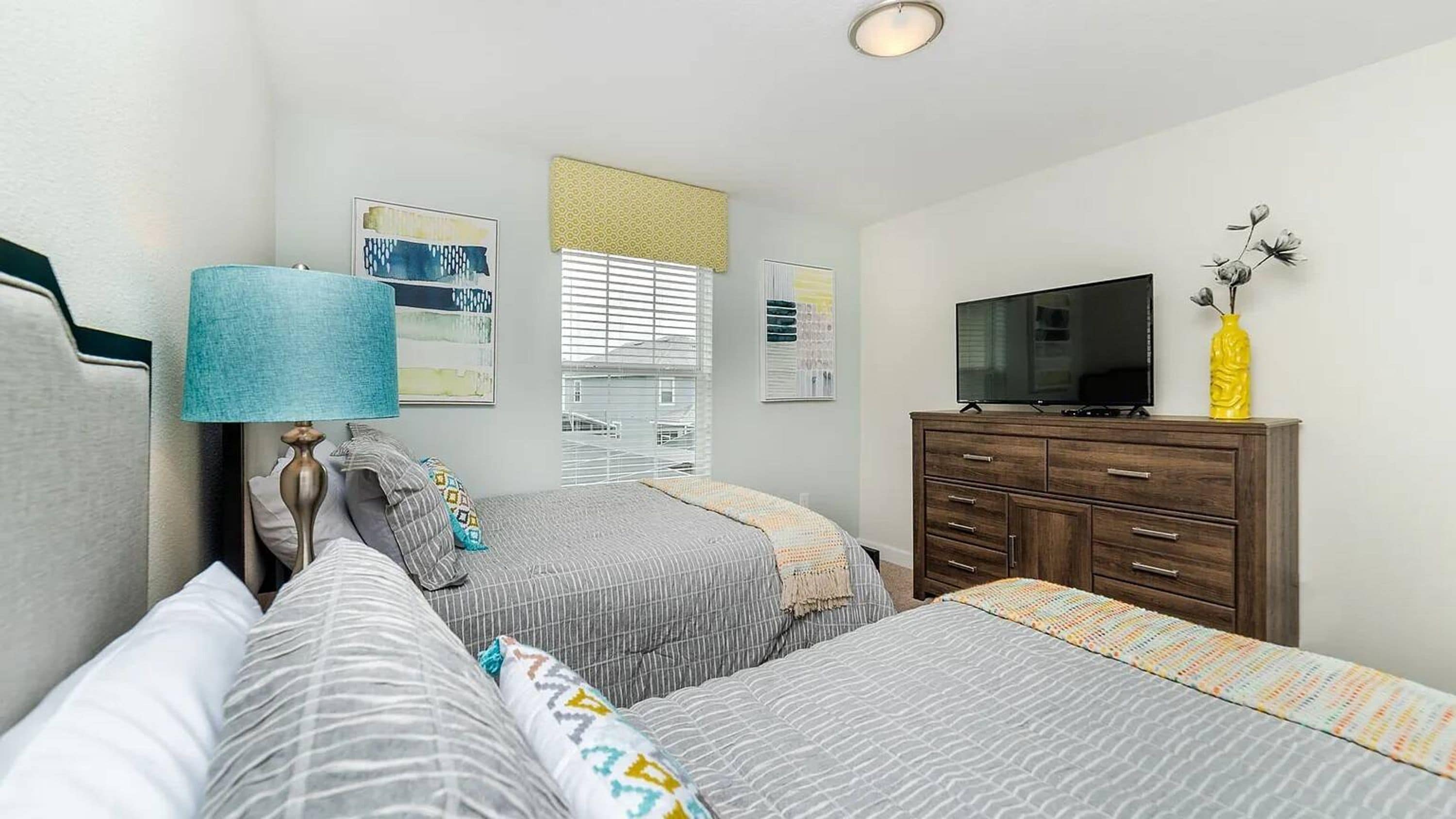 A bedroom with two beds, a TV, a dresser, and artwork on the walls.