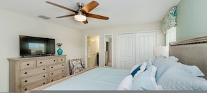 A bedroom with a bed, a dresser, a television, a ceiling fan, and a door leading to another room. - Go 43 Champions Gate (Davenport)