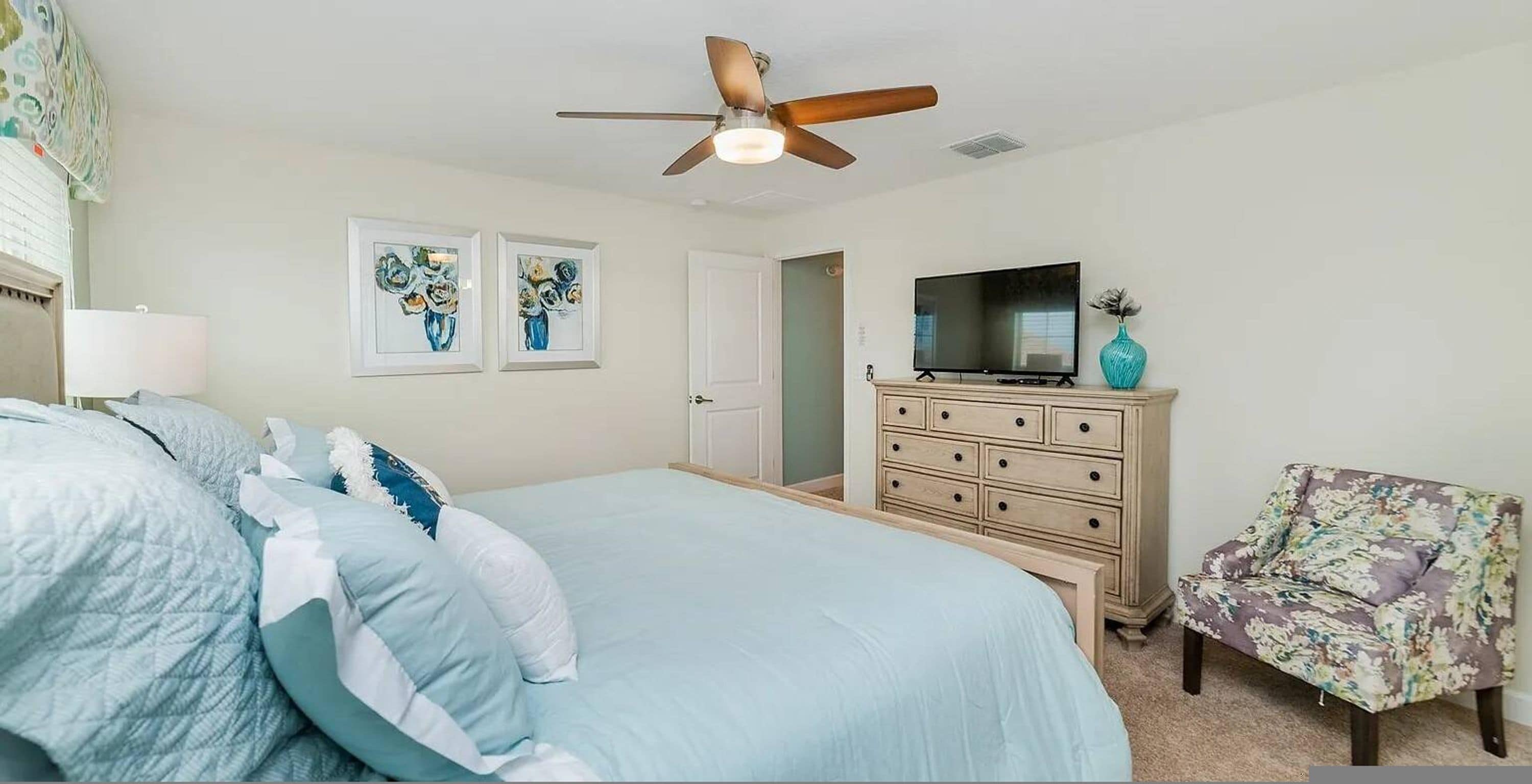 A bedroom with a bed, dresser, television, and a floral armchair.