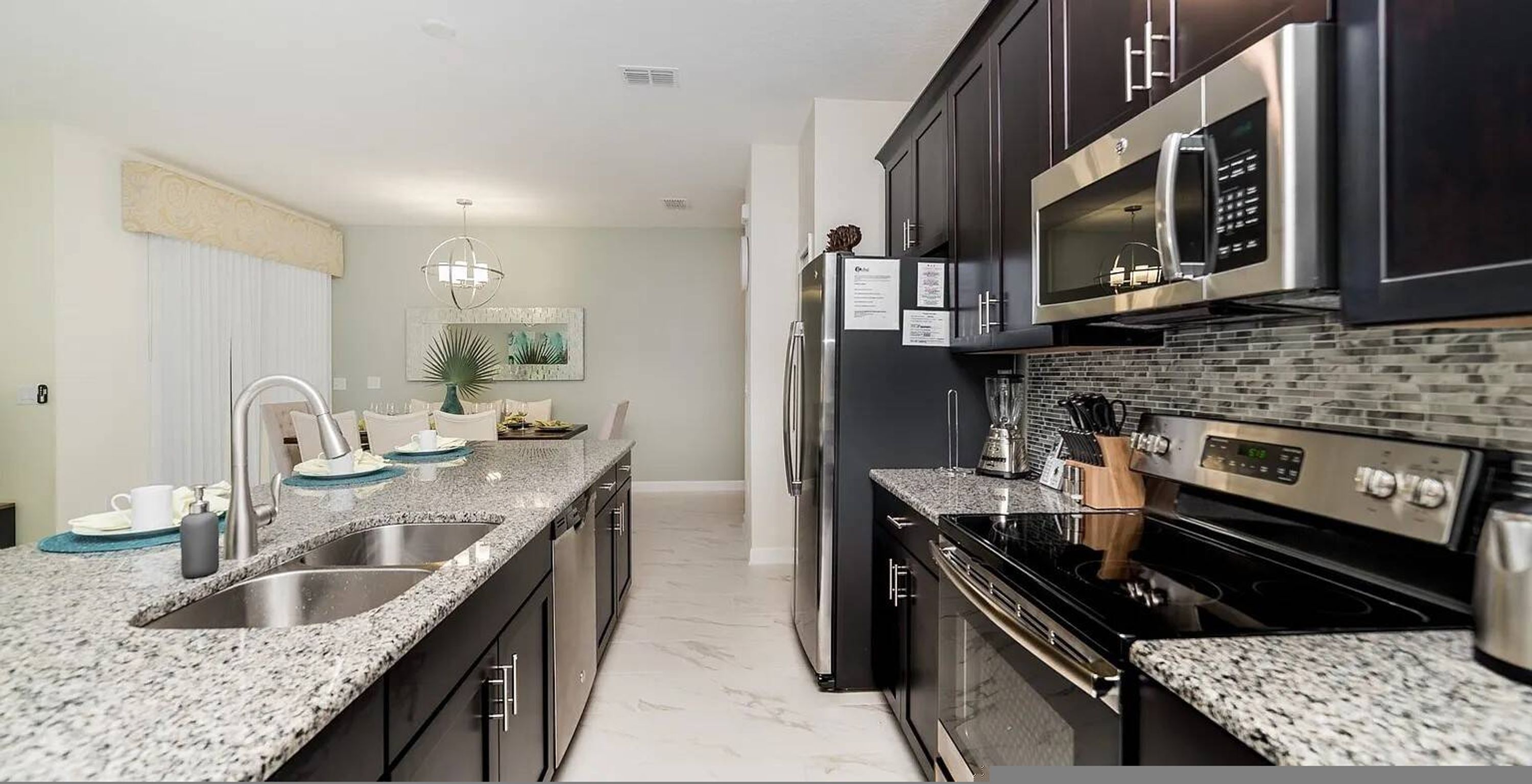 A modern kitchen with granite countertops, stainless steel appliances, and a black backsplash.