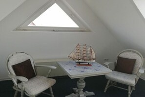 Una habitación con techo inclinado, una pequeña mesa con un modelo de barco y dos sillones tapizados.