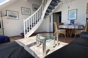 A modern living room with a glass coffee table, a staircase, and a dining area with wicker chairs. - Holiday apartment with 2 bedrooms (Wittdün)