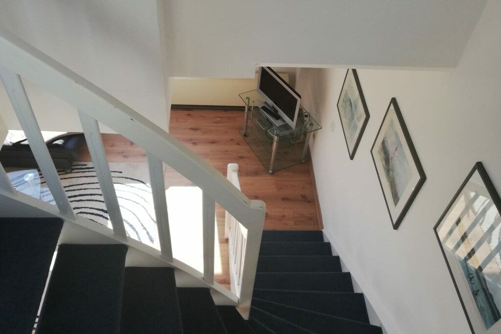 A staircase leading to a room with a television on a stand, framed pictures on the wall, and a wooden floor.