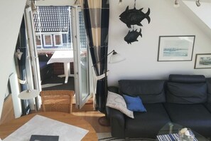 Vista interior de una habitación con un sofá de cuero negro, una mesa de centro de cristal y un comedor con mesa y sillas.