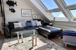 A modern living room with a sectional sofa, a glass coffee table, and a view through a skylight. - Holiday apartment with 2 bedrooms (Wittdün)