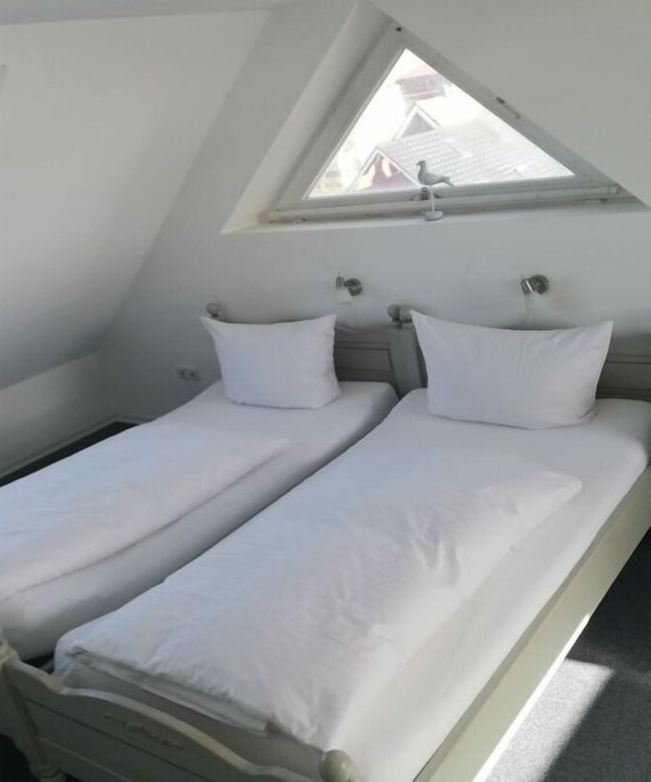 Ein Einzelbett mit weißer Bettwäsche in einem Zimmer mit geneigter Decke und einem Dachfenster.