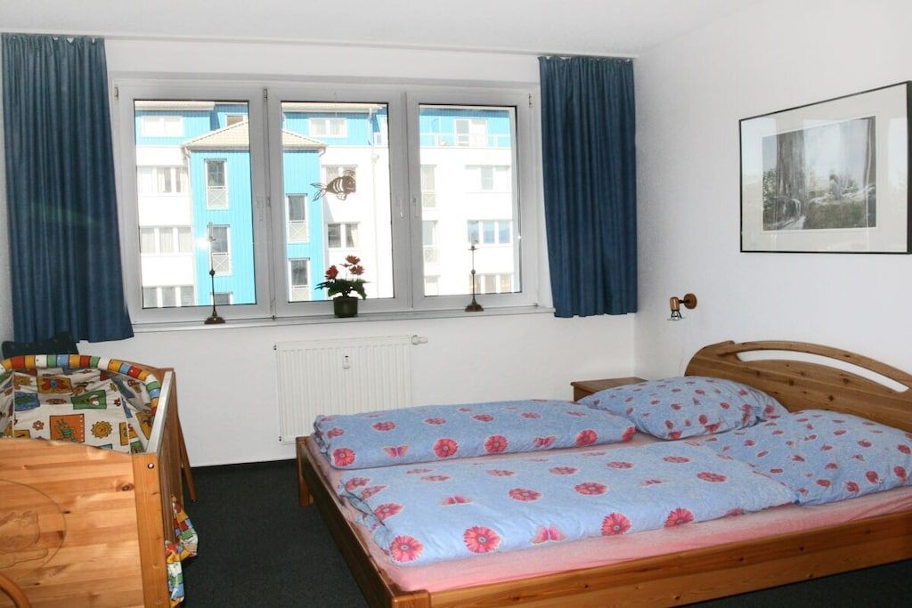 Une chambre avec un lit simple, une fenêtre avec des rideaux, un radiateur et un tableau encadré au mur.