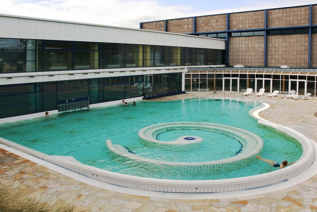 A swimming pool with a circular design, surrounded by lounge chairs and a building with large windows.